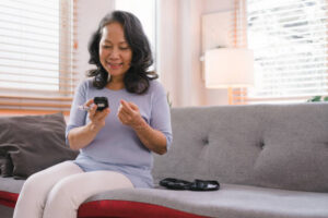 Senior checking her blood sugar level with a remote blood glucose monitoring by herself at her home